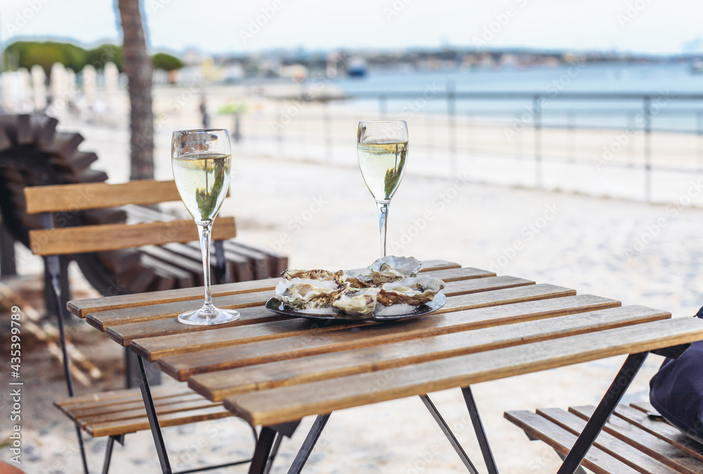 Two glasses of white wine, a plate with oysters. Beach, sea, trees on the background 