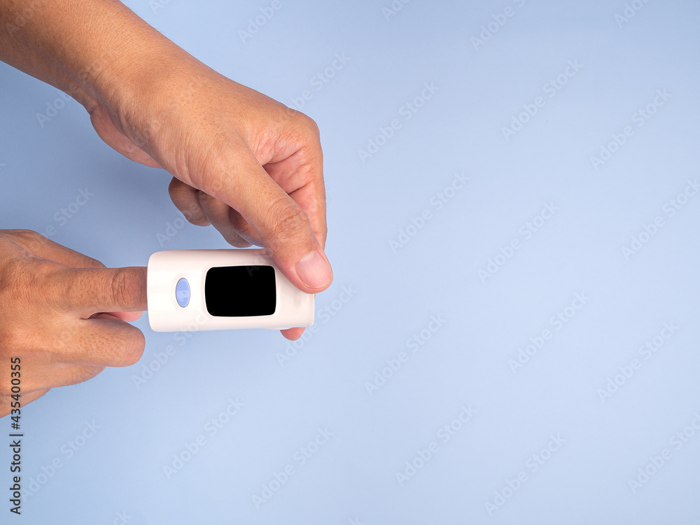 Pulse oximeter on the index finger on a light blue background. Measurement of blood oxygen and pulse. Lung disease. Close-up photo. Space for text. Healthcare concept