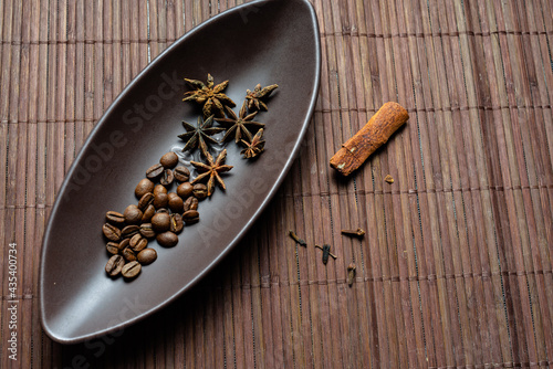Brown canoe-shaped dish on bamboo mat with coffee beans, star anise, cloves and cinnamon