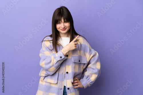 Young Ukrainian woman isolated on purple background pointing to the side to present a product