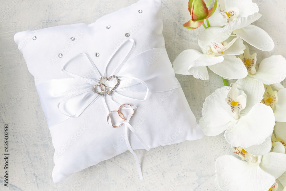 white pillow for wedding rings with rings and rhinestone hearts near white orchid on a white textured background. Wedding or engagement concept. white pillow for wedding rings with rings and rhinestone hearts near white orchid on a white textured background. Wedding or engagement concept.