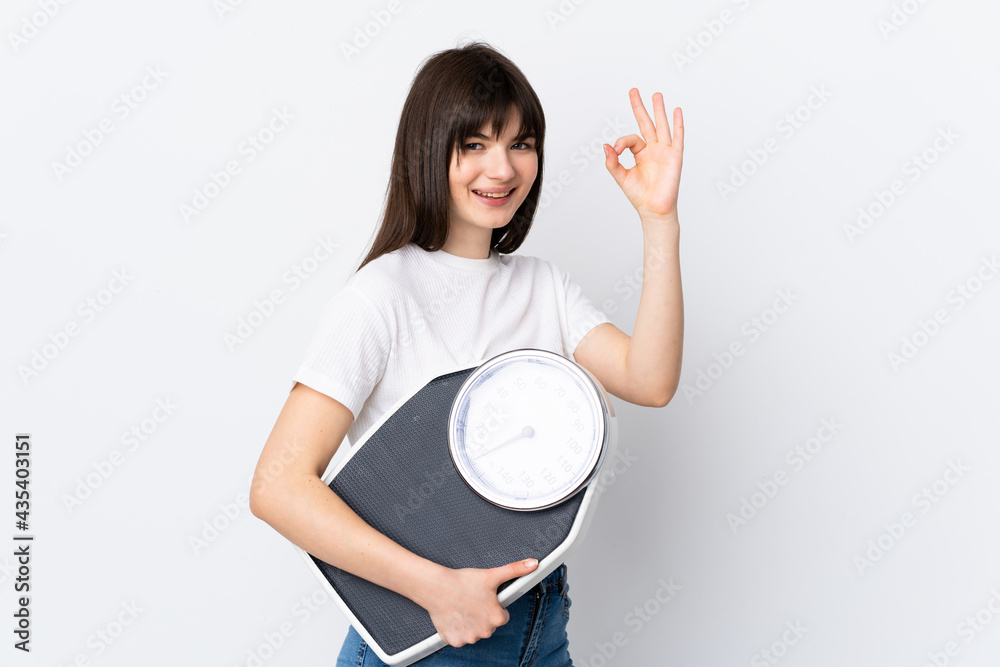 Young Ukrainian woman isolated on white background holding a weighing machine and doing OK sign Young Ukrainian woman isolated on white background holding a weighing machine and doing OK sign