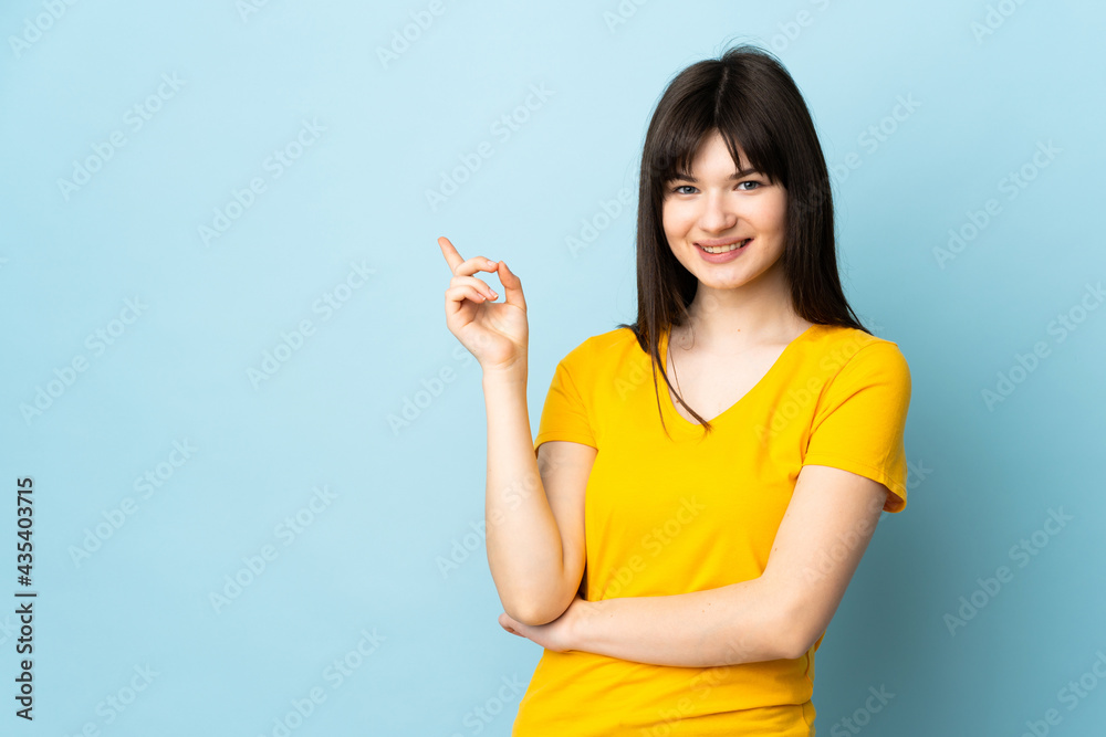 Teenager Ukrainian girl isolated on blue background happy and pointing up Teenager Ukrainian girl isolated on blue background happy and pointing up