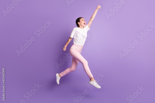 Full length photo of excited carefree girl raise hand fist look up empty space isolated on violet color background