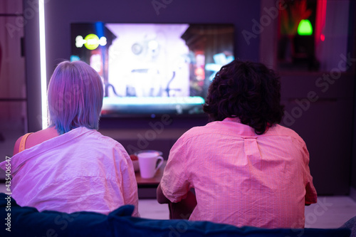 Beautiful blue haired girl and young guy holding gaming contorllers playing video games at home.