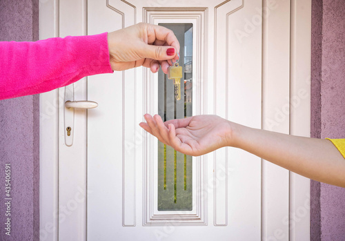 hand giving key to another hand in front of the door
 photo