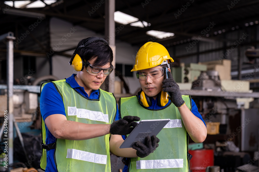 Asian factory male worker discussing and work with tablet for maintenance machine lathe metal in the industry factory. Engineer worker using manual document for lathe machine in the factory Asian factory male worker discussing and work with tablet for maintenance machine lathe metal in the industry factory. Engineer worker using manual document for lathe machine in the factory