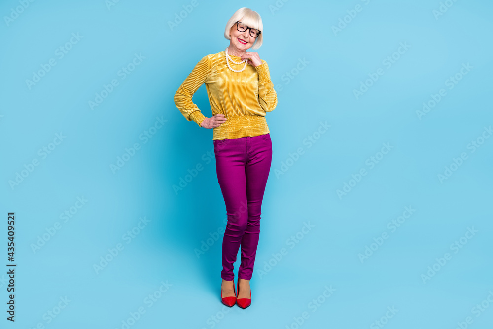 Full size photo of nice short hairdo elder lady stand wear blouse eyewear pants isolated on blue color background Full size photo of nice short hairdo elder lady stand wear blouse eyewear pants isolated on blue color background