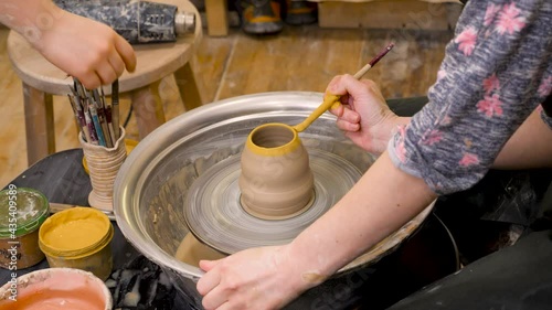 Pottery painting on clay pot. Handmade workshop ceramic. Earthenware. Painting ceramic pot with paint brush in pottery class potter workshop wheel. Potter work hands close up painting pottery making