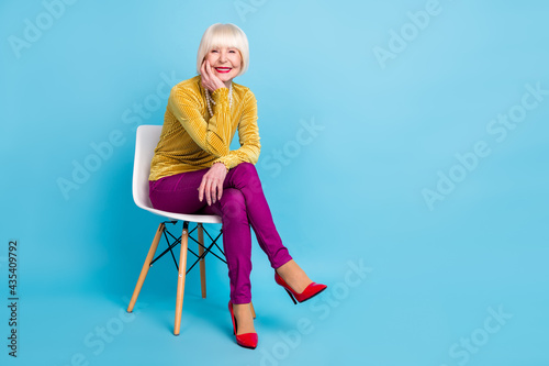 Full length photo of positive short hairdo aged lady sit wear blouse pants isolated on blue color background