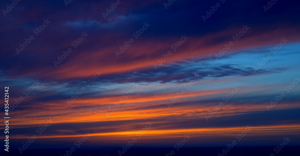 Beautiful orange bright sunset. The clouds are painted in the colors of the sunset and the blue sky Beautiful orange bright sunset. The clouds are painted in the colors of the sunset and the blue sky