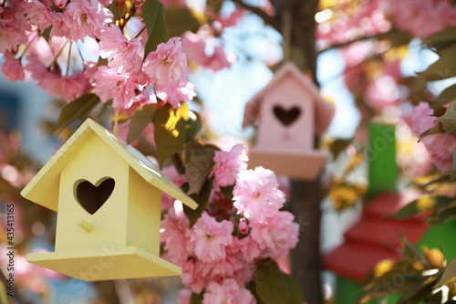 Yellow bird house with heart shaped hole hanging on tree branch outdoors