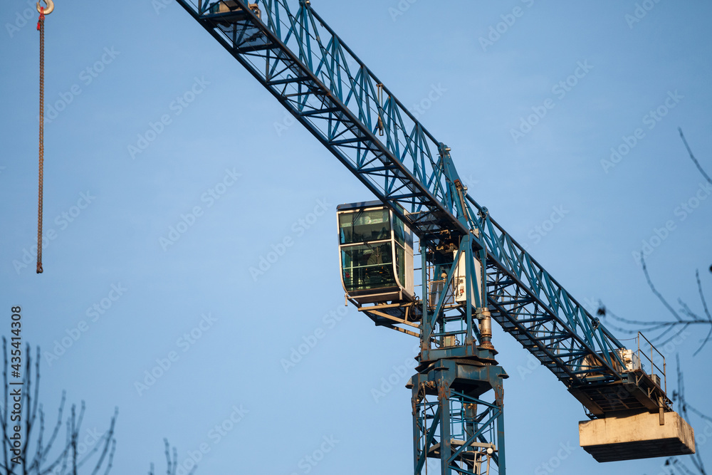 Blue metal crane in front of a building being assembled in a construction site taken from below during a sunny afternoon, under a blue sky... Blue metal crane in front of a building being assembled in a construction site taken from below during a sunny afternoon, under a blue sky...