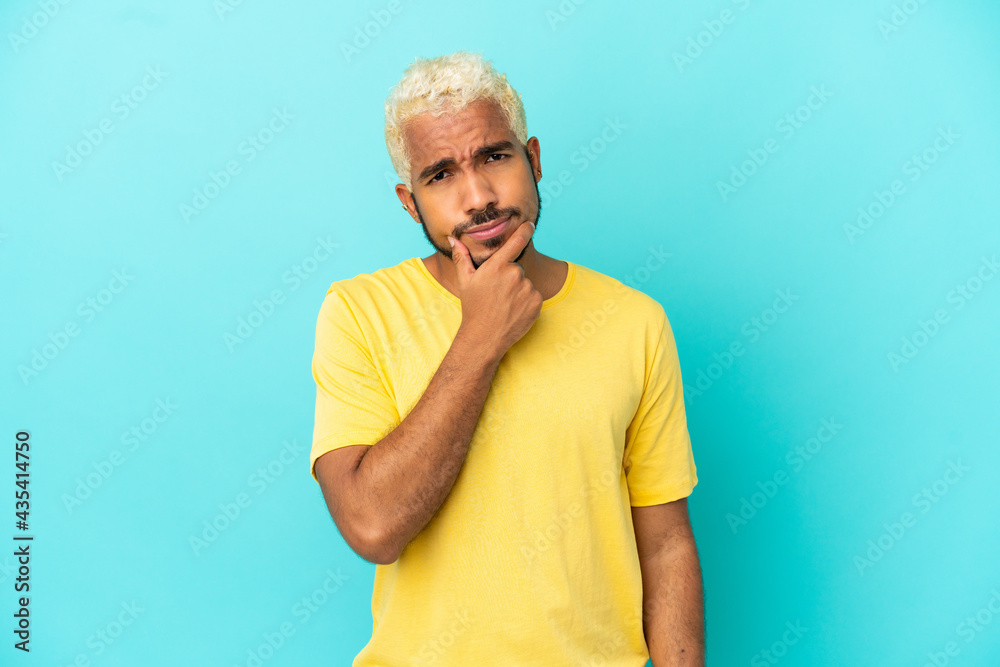 Young Colombian handsome man isolated on blue background having doubts Young Colombian handsome man isolated on blue background having doubts