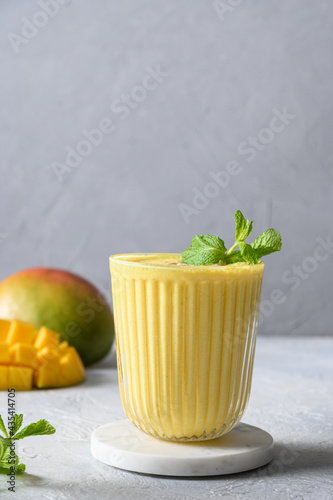 Indian ayurvedic mango lassie or smoothie on light gray background. Close up. Traditional healthy vegan beverage with mango. Freshness lassi made of yogurt, water, spices, fruits and ice.