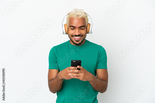 Young Colombian handsome man isolated on white background listening music and looking to mobile © luismolinero