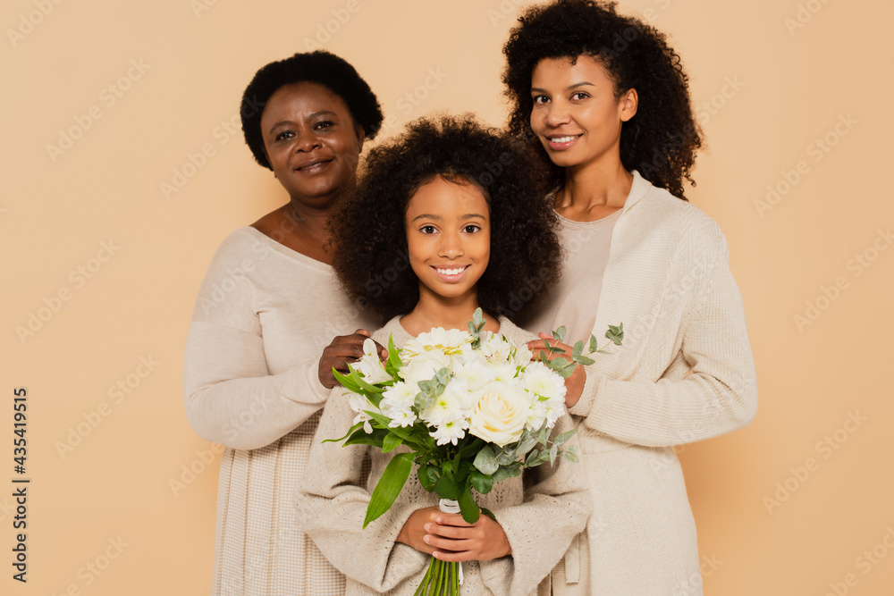 happy family of african american grandmother, daughter and granddaughter with bouquet of flowers isolated on beige happy family of african american grandmother, daughter and granddaughter with bouquet of flowers isolated on beige