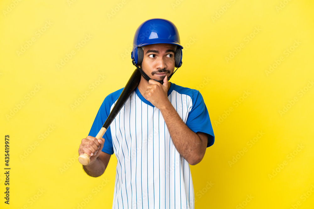 Young Colombian latin man playing baseball isolated on yellow background having doubts and thinking