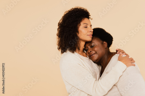 Valokuvatapetti african american adult daughter hugging middle aged mother with closed eyes isol