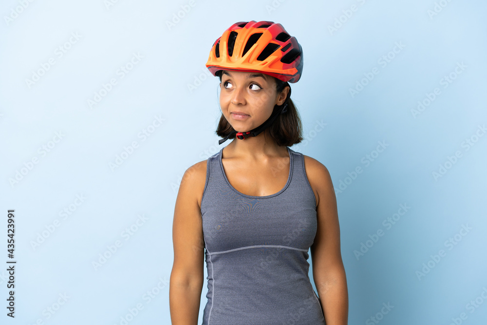Young cyclist woman isolated on blue background making doubts gesture looking side Young cyclist woman isolated on blue background making doubts gesture looking side
