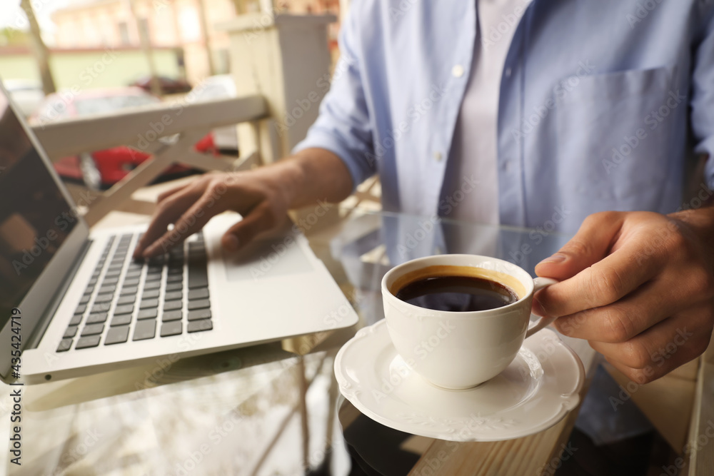 Man with cup of coffee working on laptop at outdoor cafe in morning, closeup Man with cup of coffee working on laptop at outdoor cafe in morning, closeup