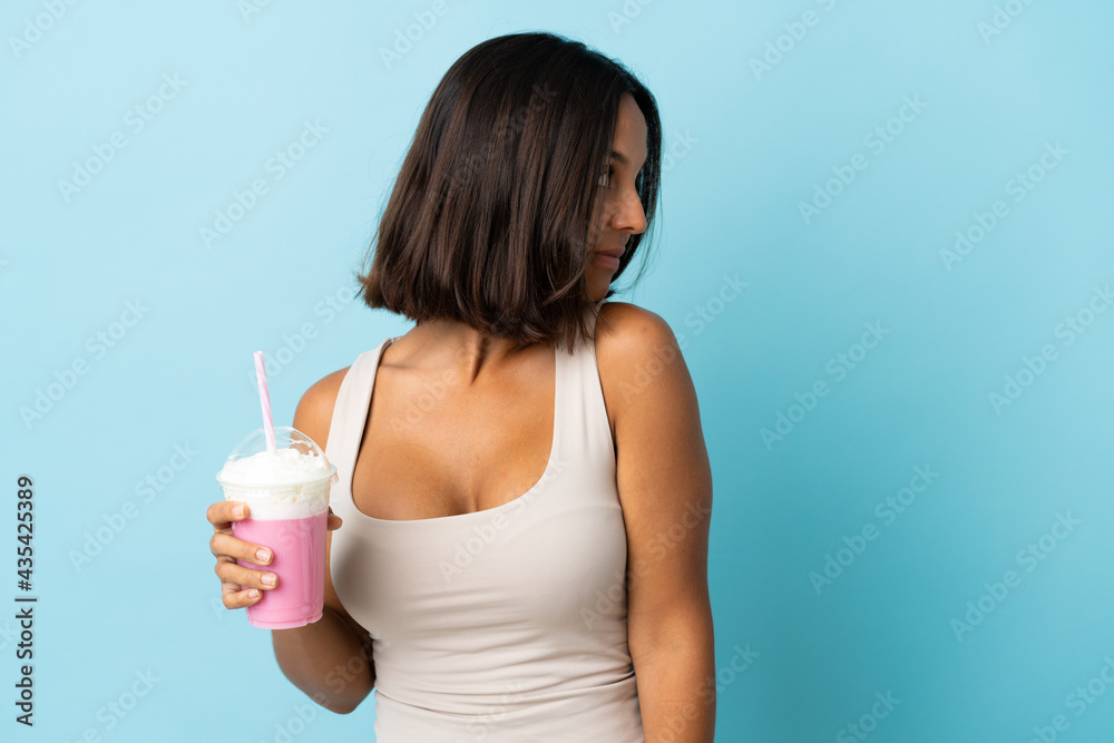 Young woman with strawberry milkshake isolated on blue background . Portrait Young woman with strawberry milkshake isolated on blue background . Portrait