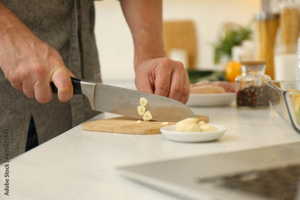 Man cutting garlic while watching online cooking course via laptop in kitchen, closeup Man cutting garlic while watching online cooking course via laptop in kitchen, closeup