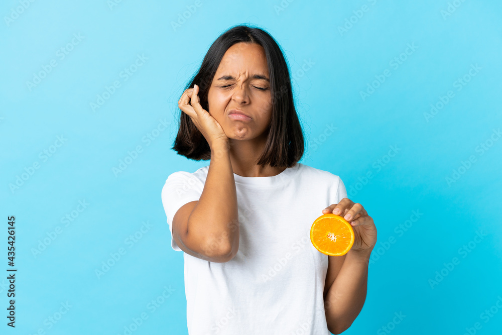 Young asian girl holding an orange isolated on blue background frustrated and covering ears Young asian girl holding an orange isolated on blue background frustrated and covering ears