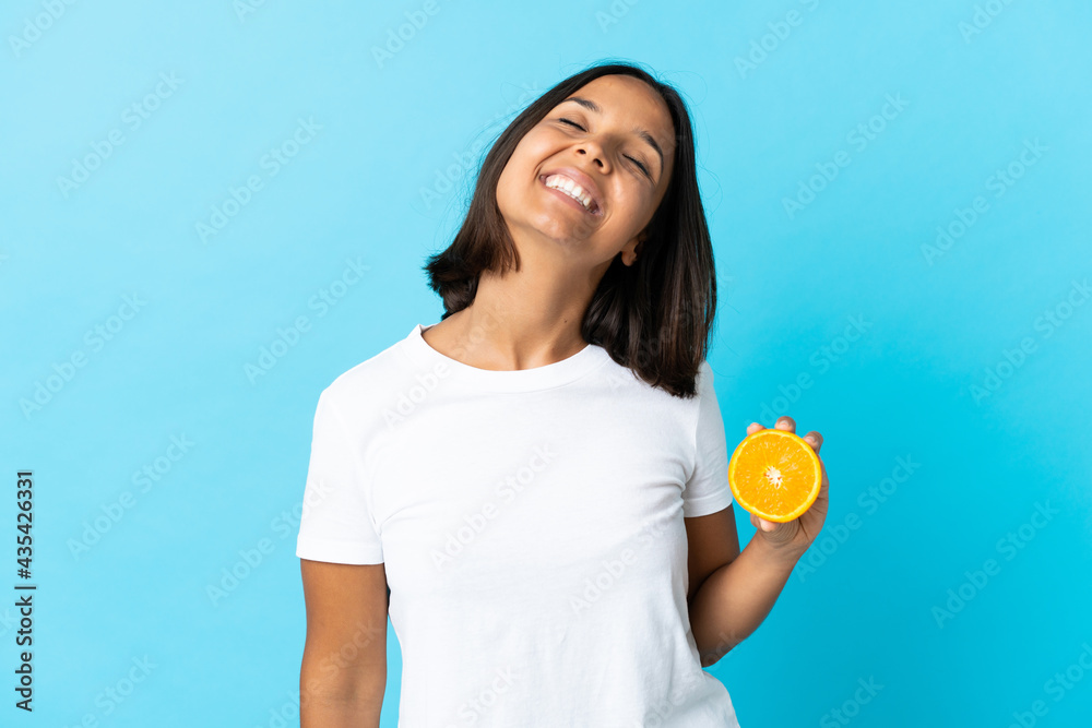 Young asian girl holding an orange isolated on blue background laughing Young asian girl holding an orange isolated on blue background laughing