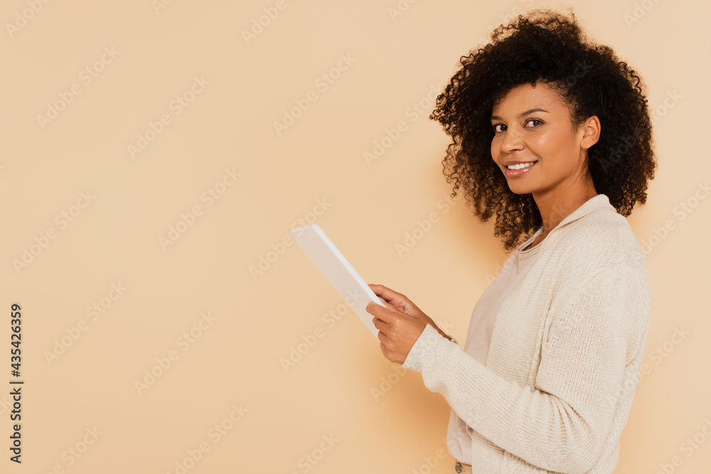 smiling african american woman with digital tablet isolated on beige smiling african american woman with digital tablet isolated on beige