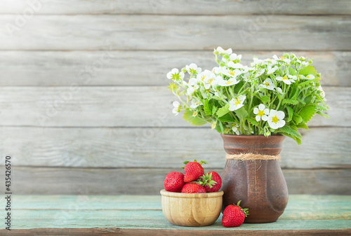 Summer background with strawberrires in the bowl and white flowers in the vase on the wooden backdrop	