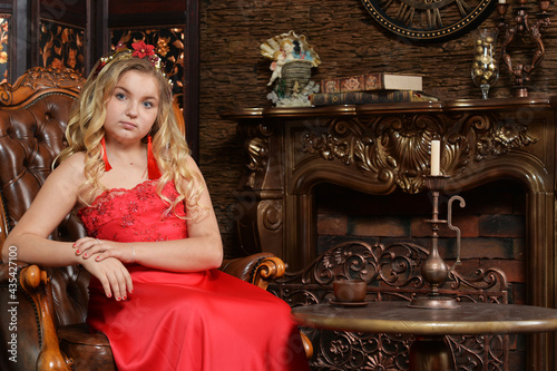 Blonde teenage girl in bright red dress sitting in armchair photo