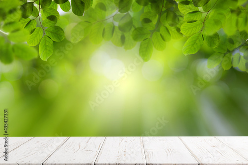 Empty white wooden table with green leaves, bokeh and sun light with copy space for text ,Template mock up for display of product. green nature and ecology concept.