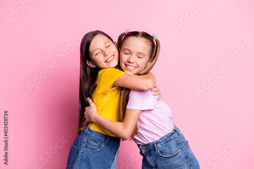 Portrait of attractive kind dreamy cheerful pre-teen girls hugging isolated over pink pastel color background