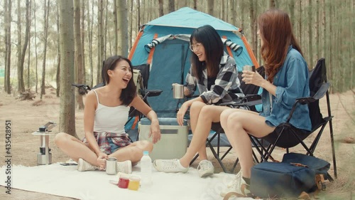 Group of young asia camper friends sitting in chairs by tent in forest. Teenager girl traveler relax and talk on a summer day at campsite. Outdoor activity, adventure travel, or holiday vacation.