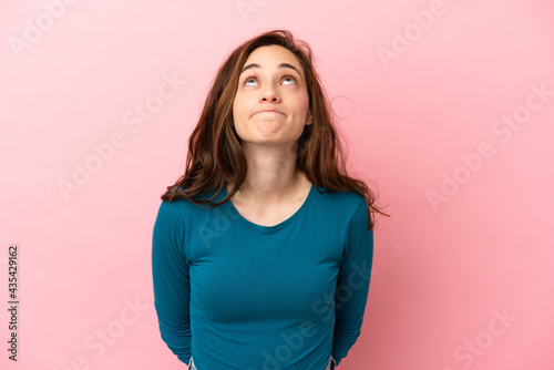 Young caucasian woman isolated on pink background and looking up