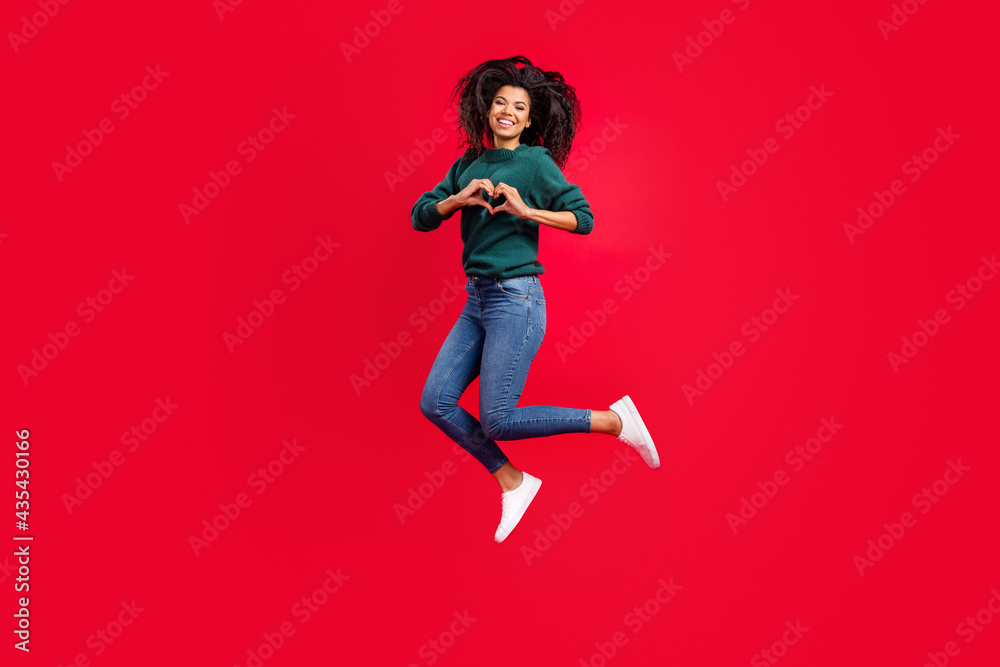 Photo of sweet charming dark skin woman dressed green pullover smiling showing fingers heart jumping isolated red color background