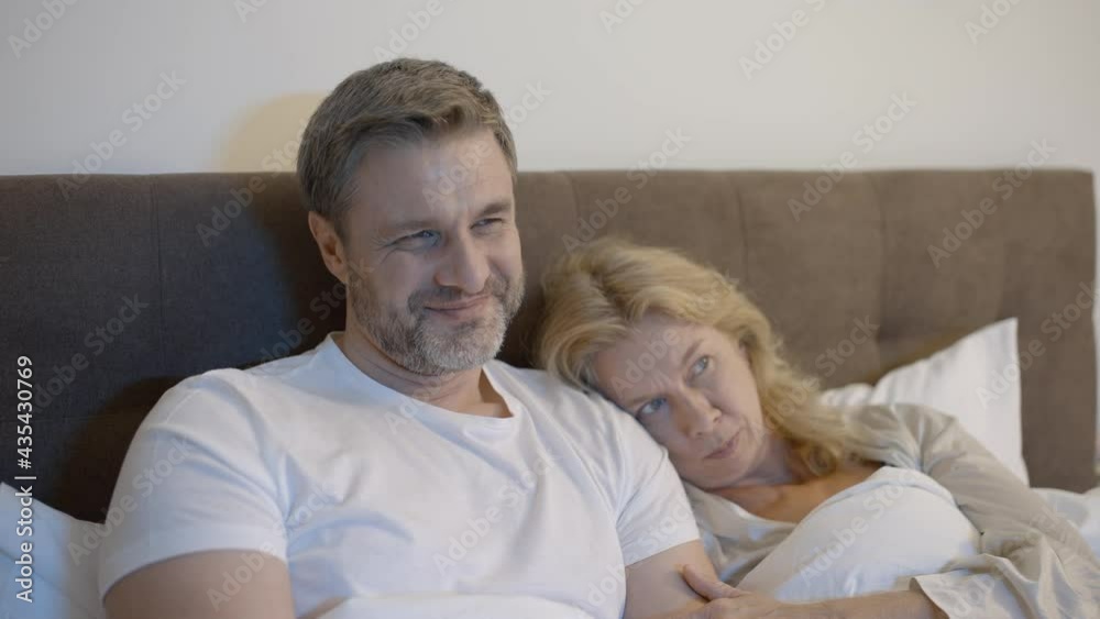 Adult couple watching horror movie in bed together, scared wife hugging husband Adult couple watching horror movie in bed together, scared wife hugging husband
