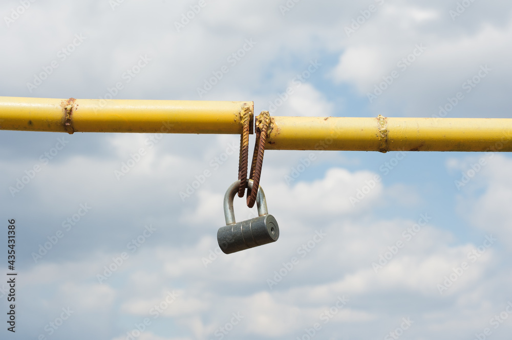 Old, rusty, yellow entrance barrier closed by a padlock Old, rusty, yellow entrance barrier closed by a padlock