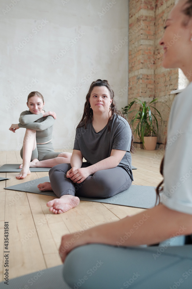 Young disable female with Down syndrome looking at yoga trainer during consultation while having break