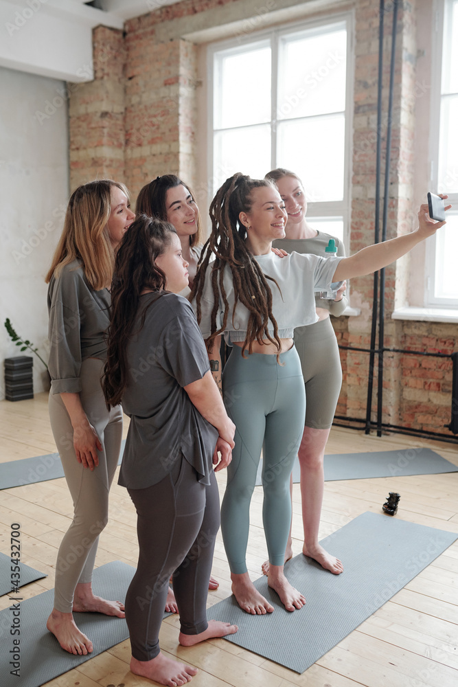 Obraz premium Girls in activewear standing on the floor of gym and making selfie after workout
