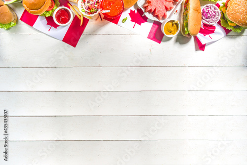 Set of various Canada Day bbq food. Picnic party table with maple leaf shaped watermelon, flags, burgers, hot dogs, fries and sauces, cold drinks, white table with red decor, top view copy space