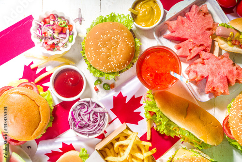 Set of various Canada Day bbq food. Picnic party table with maple leaf shaped watermelon, flags, burgers, hot dogs, fries and sauces, cold drinks, white table with red decor, top view copy space