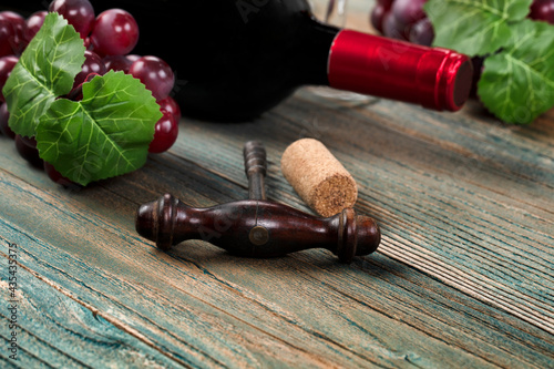 Selective focus of vintage corkscrew with wine bottle and grapes in background on blue rustic wood table