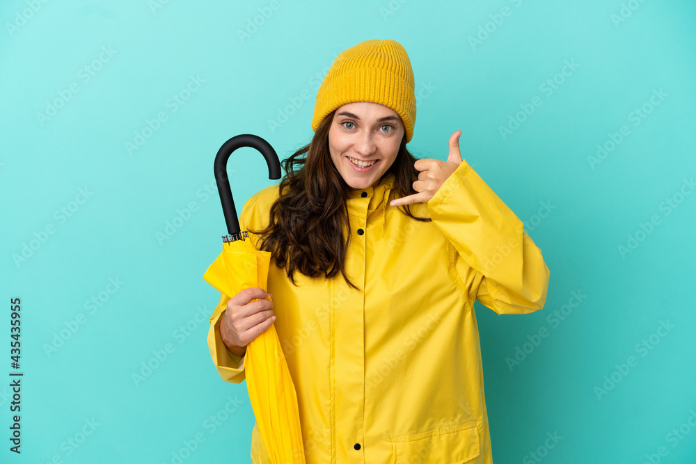 Young caucasian man holding an umbrella isolated on blue background making phone gesture. Call me back sign
