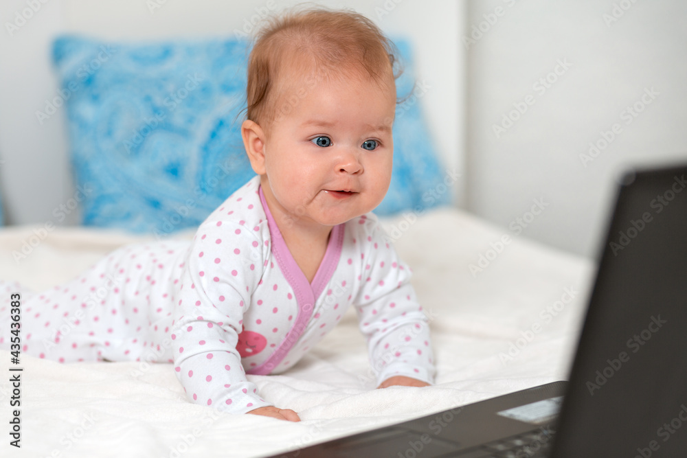 Happy baby in sliders is lying on the bed and watching cartoons on a laptop. The concept of entertainment and education for children using the Internet Happy baby in sliders is lying on the bed and watching cartoons on a laptop. The concept of entertainment and education for children using the Internet
