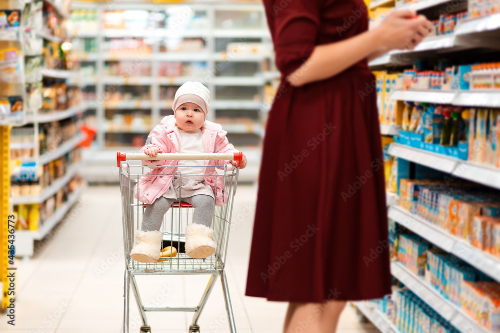 Shopping. A toddler sits in a grocery cart and looks around while his mother picks out groceries. Family shopping in the supermarket