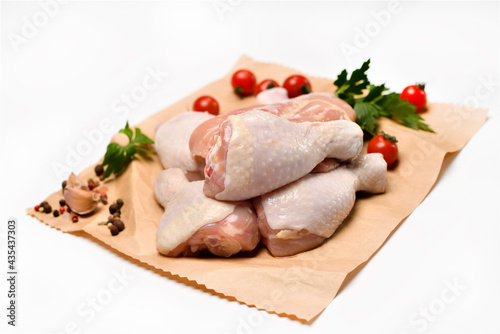 Fresh raw chicken legs with ingredients for cooking on a wrapping paper on white background