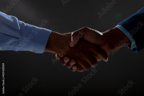Mid section of two businessmen shaking hands against black background