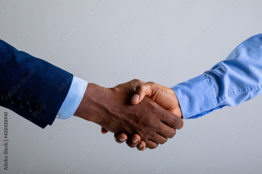 Mid section of two businessman shaking hands against grey background